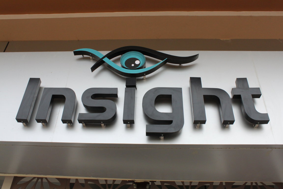 Close-up of the Insight Institute signage, dimensional dark metal letters crowned by the brand's stylised teal-and-black eye emblem